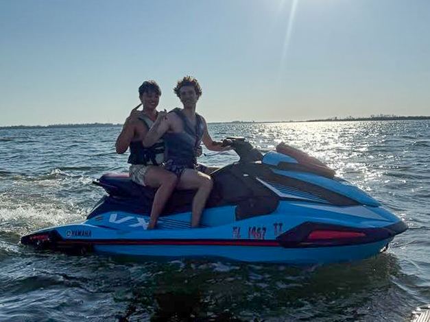 Two brothers riding a jet ski on open water