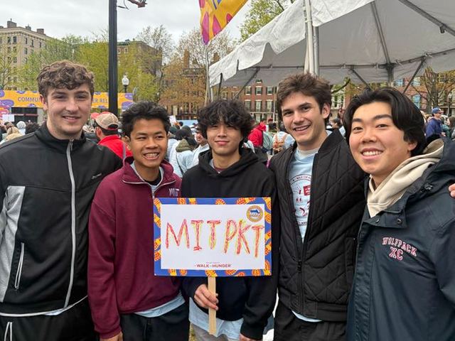 Brothers holding an MIT Phi Kappa Theta sign outdoors